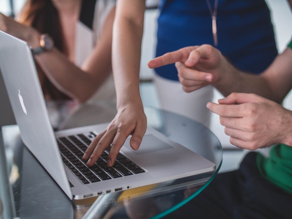 People pointing at a laptop screen while troubleshooting SharePoint Online and OneDrive sync delays